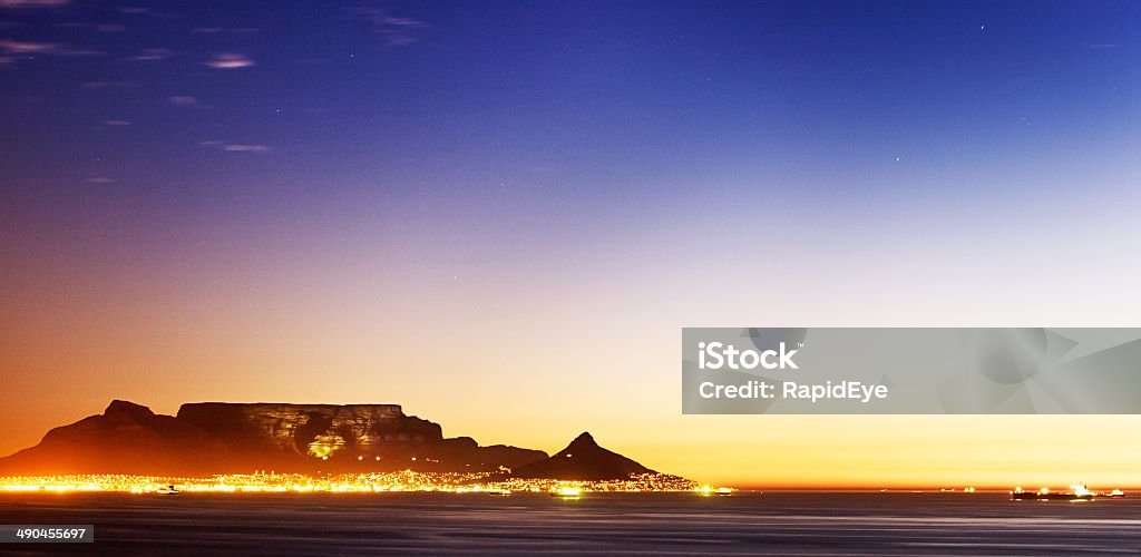 Table Mountain twilight Just after sunset, Cape Town lights come on at the foot of the famous Table Mountain. This shot taken from Sunset Beach, Milnerton. Copy space on the darkening sky. Sunset Beach - Hawaii Stock Photo