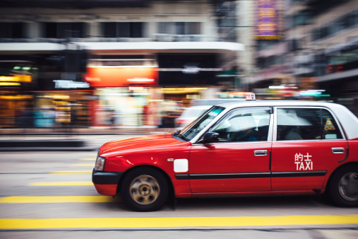 An action shot of a taxi driving through downtown Hong Kong city, depicting the rushed pace of city life.  Horizontal image with copy space.