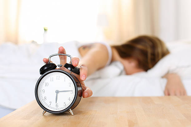 sleepy joven mujer tratando de forma reloj despertador - despertador fotografías e imágenes de stock