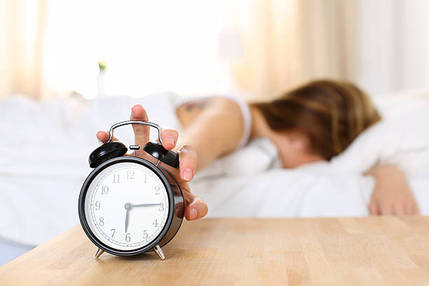 Sleepy young woman trying kill alarm clock Sleepy young woman trying kill alarm clock while bury face in pillow. Early wake up, not getting enough sleep, getting work concept. Female stretching hand to ringing alarm willing turn it off alarm clock stock pictures, royalty-free photos & images