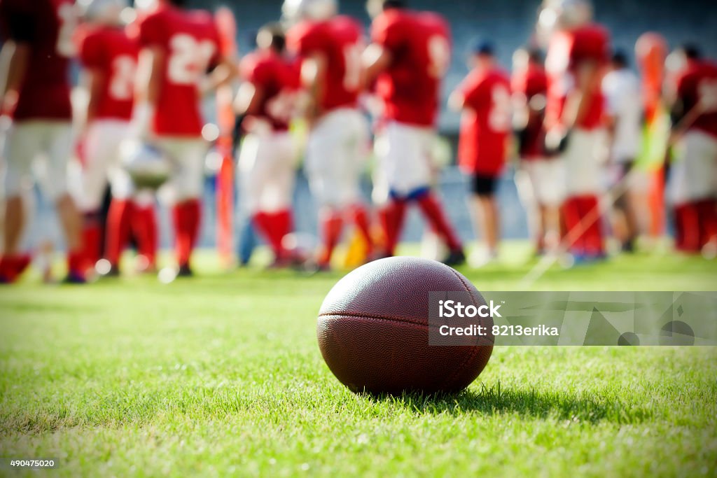 Close up on an american football ball Close up of an american football on the field, players in the background College American Football Stock Photo