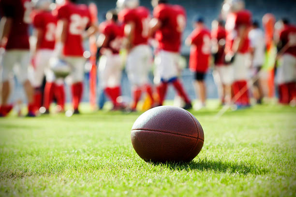 Close up on an american football ball Close up of an american football on the field, players in the background american football sport stock pictures, royalty-free photos & images