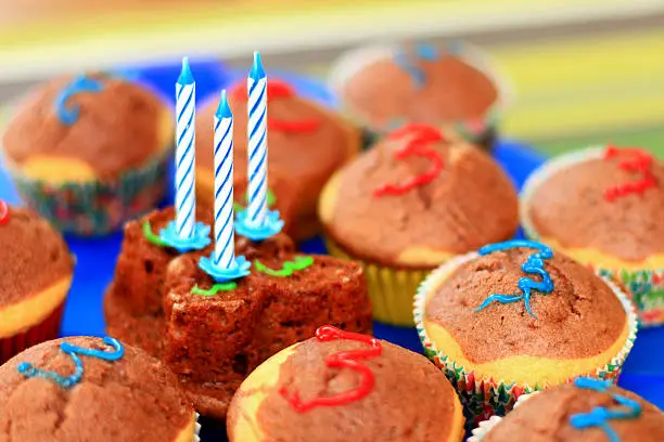 Group of colorful birthday muffins for the third birthday party including some decoration. Three candles on top of the center muffin, which is in in the shape of a butterfly. With shallow depth of field.