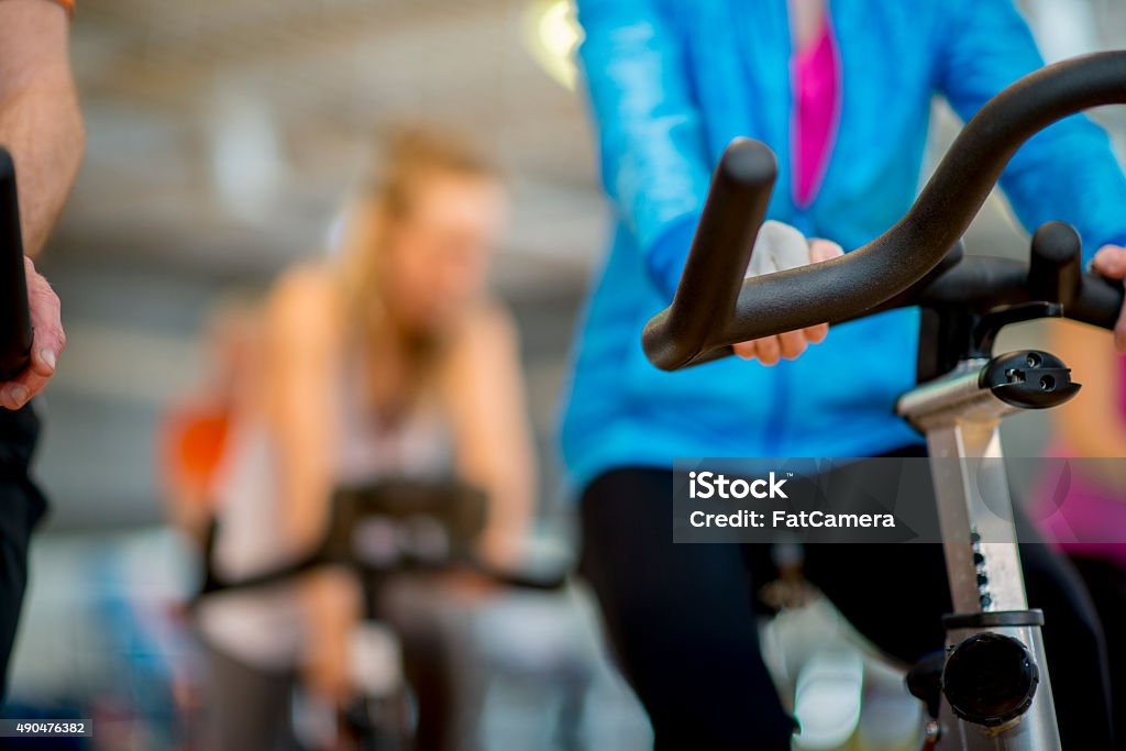 Women in a Cycling Fitness Class A group of individuals are working out together at a exercise class. They are sitting on their stationary bikes and and cycling together to the music. Cycling Stock Photo