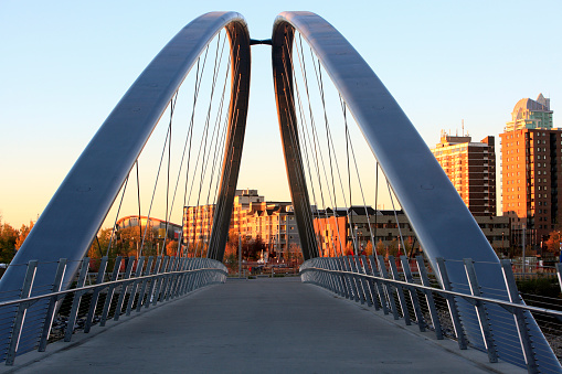 New foot bridge over the Bow River in the East Village.  Saddledome and condos can be seen through bridge. Fall season.