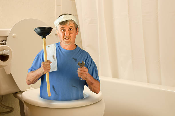 Humorous do-it-yourself plumber with a funny confused look on his face is inside a toilet with his tools and toilet paper draped over him.