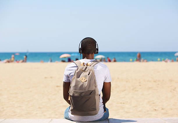 homem sentado na praia, ouvir música em auscultadores - men beach back rear view imagens e fotografias de stock