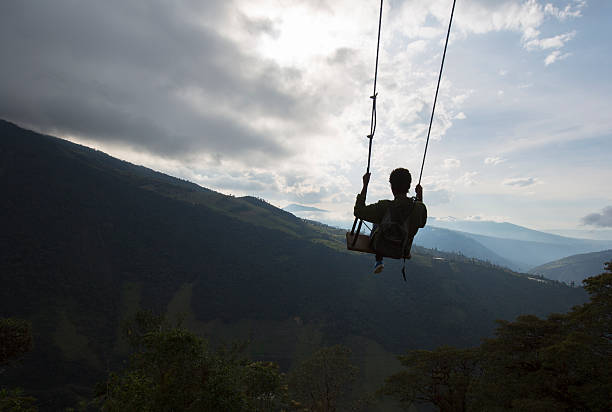 Swing at the Casa del Arbol in Banos, Ecuador Banos, Ecuador - February 20, 2015: Silhouette of happy young man on a swing with a fantastic mountain view at the Casa del Arbol, Ecuador mt tungurahua sunset mountain volcano stock pictures, royalty-free photos & images