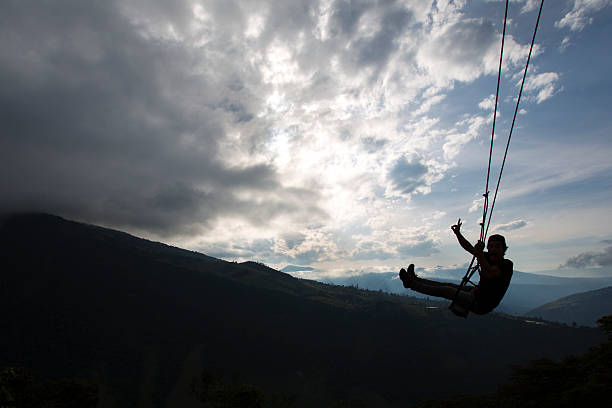 Swing at the Casa del Arbol in Banos, Ecuador Banos, Ecuador - February 20, 2015: Silhouette of happy young man on a swing with a fantastic mountain view at the Casa del Arbol, Ecuador mt tungurahua sunset mountain volcano stock pictures, royalty-free photos & images