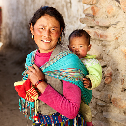 Tibetan woman carrying her baby, Upper Mustang. Mustang region is the former Kingdom of Lo and now part of Nepal,  in the north-central part of that country, bordering the People's Republic of China on the Tibetan plateau between the Nepalese provinces of Dolpo and Manang. The Kingdom of Lo, the traditional Mustang region, and “Upper Mustang” are one and the same, comprising the northern two-thirds of the present-day Nepalese Mustang District, and are well marked by official “Mustang” border signs just north of Kagbeni where a police post checks permits for non-Nepalese seeking to enter the region, and at Gyu La (pass) east of Kagbeni.http://bem.2be.pl/IS/mustang_380.jpg