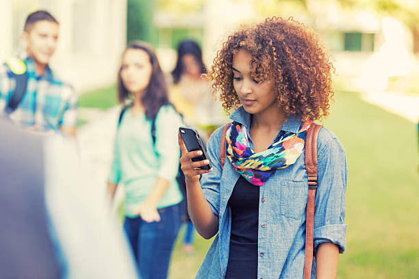 linda estudante do ensino médio usando telefone inteligente ao ar livre - african ethnicity standing college student curly hair - fotografias e filmes do acervo