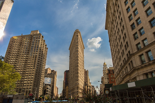 Busy day in New York by the Flatiron Building. Horizontal, low angle street view. Beautiful big city architecture of a famous landmark building exterior in New York City. Clouds, clocks and buildings in a famous place. 