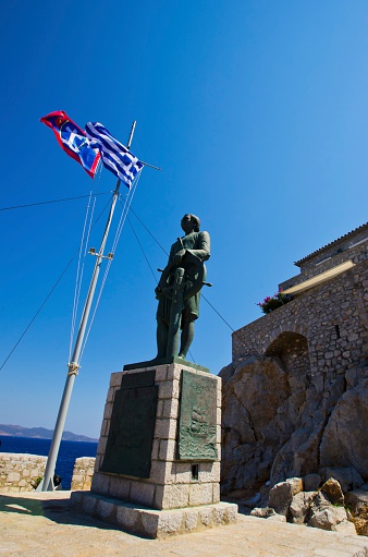 Hydra, Greece: 18 August 2012 - The statue of Andreas Miaoulis, a hero of the Greek war of independence, which is a landmark of the Greek island, Hydra. On the background the flag of Hydra and Greece.