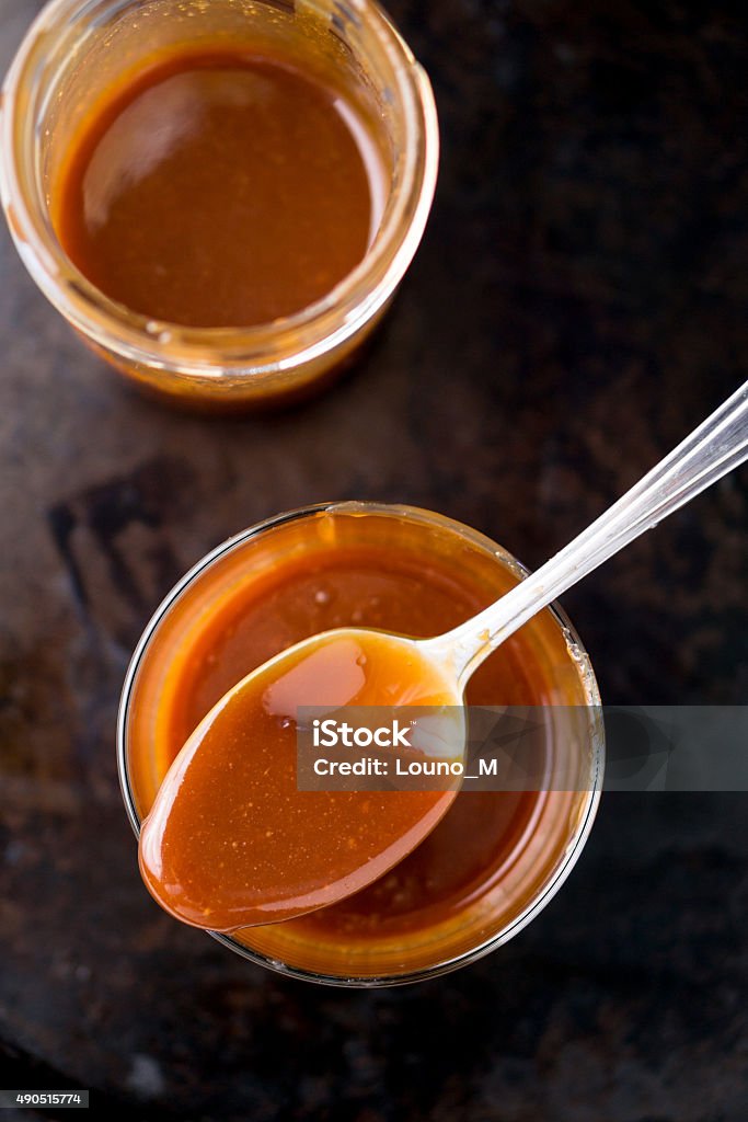 Jars of Caramel Sauce With a Spoon Homemade caramel sauce slowly dripping in a glass jar. This delicious caramel sauce can be used as topping to add flavor to cakes, ice cream and many other desserts. Caramel Stock Photo