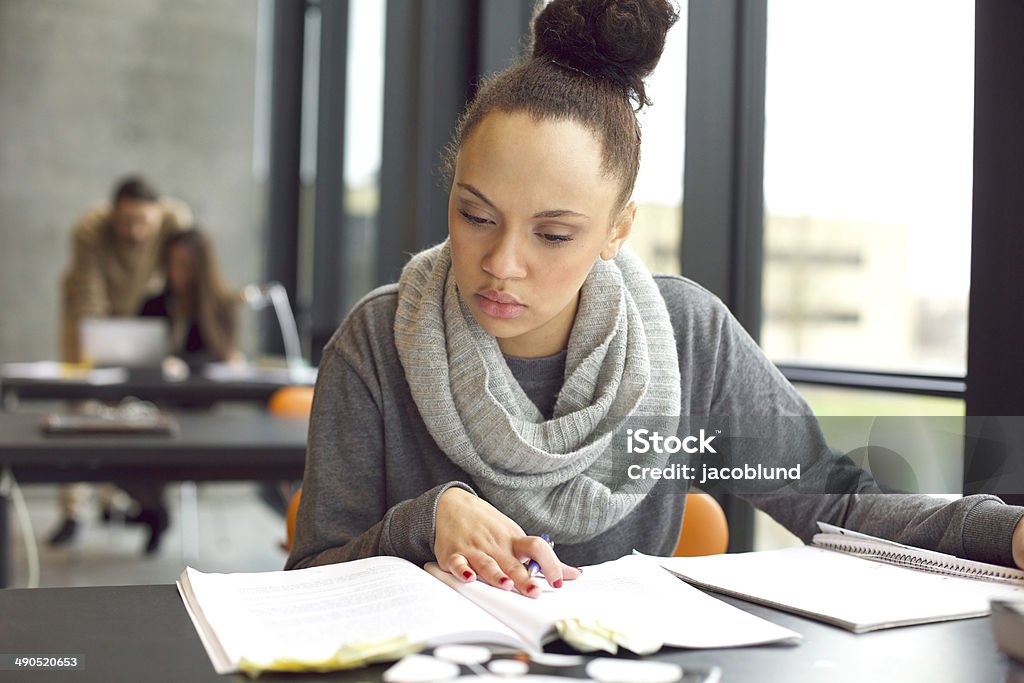 Female student studying in a library Female student reading a book for finding information. Young african american woman sitting at table doing assignments in university library. Educational Exam Stock Photo