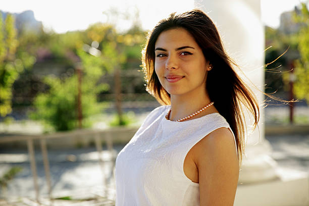 Portrait of beautiful young woman with brown hair looking at camera standing outside in the city on a summer day
