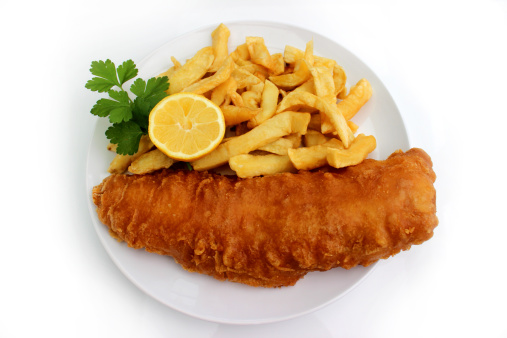 Image of take away fish and chips served on a white plate, consisting of battered cod, chipped potatoes, lemon and parsley.