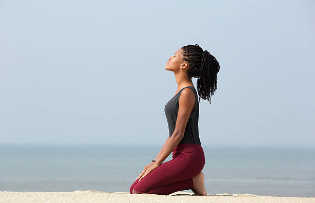 Woman meditating at the beach Portrait of a beautiful young african american woman meditating at the beach enjoying summer kneeling stock pictures, royalty-free photos & images