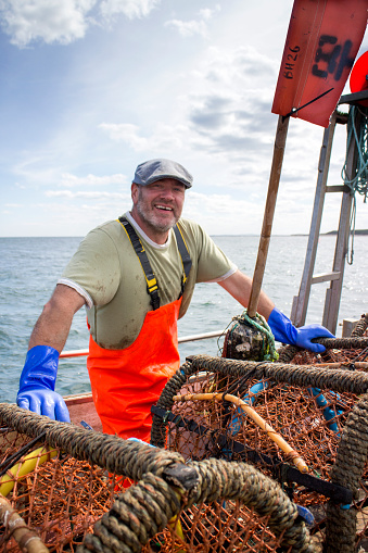 Fisherman with fresh fish on the fishing boat deck, posing with a fisherman beanie. He holds a box of mackerel