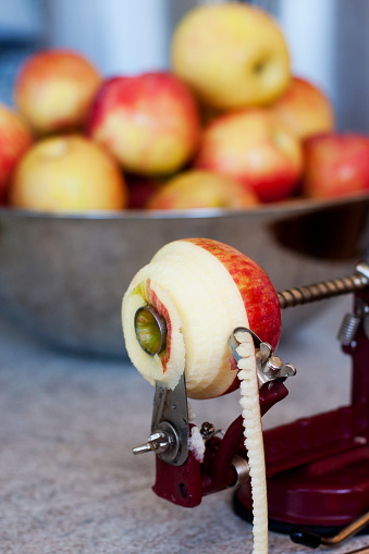 Peeling/coring/slicing an apple with an old-fashioned, hand-crank apple peeler/corer/slicer with a bowl of apples in the background.