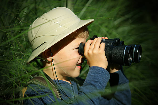 istock Child in Pith Helmet Hiding in Grass Looking Through Binoculars 490546116