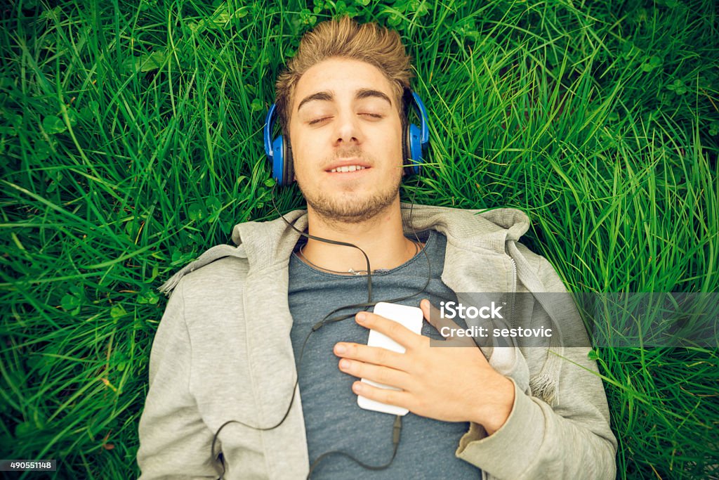 Young man with headphones lying down in the grass Young man relaxing outside , listening to music, lying down in the grass Flower Stock Photo