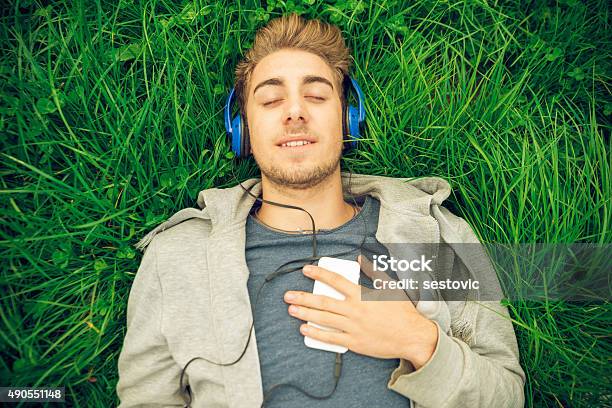 Young Man With Headphones Lying Down In The Grass Stock Photo - Download Image Now - Flower, Grass, Lying Down