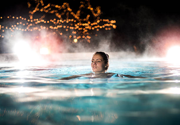 Beautiful woman swimming in a swimming pool with steam. Young woman enjoying in a heated swimming pool at night. thermal pool stock pictures, royalty-free photos & images
