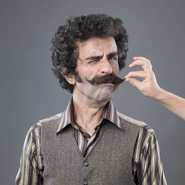 Woman Hand Pulling Up Adult Man's Handlebar Moustache Woman Hand Pulling Up Adult Man's Handlebar Moustache.The model is wearing a striped shirt and a waist.He has curly hair.Woman hand is on the right side of square frame.The background is gray.The image was shot with a medium format camera Hasselblad H4D in studio. women movember mustache facial hair stock pictures, royalty-free photos & images