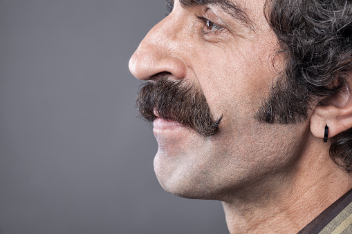 Close up photo of handlebar mustaches of smiling man on gray background.The model is on the right side of frame and faced to blank gray left side.Side view of model is seen.He is smiling.The hair color is brown.Little part of eyebrows and down is seen.The photo was shot with a full frame DSLR camera in studio.