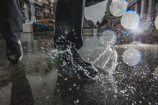 Unrecognizable human foot splashing water in a puddle on a rainy day in the city.