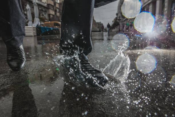 pessoa irreconhecível entrar em uma poça durante o dia chuvoso. - business human foot shoe men - fotografias e filmes do acervo