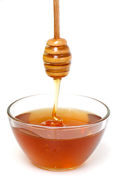 Honey dripping from a wooden dipper on white background