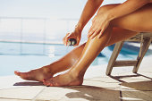 Woman spraying suntan lotion onto her leg by the pool