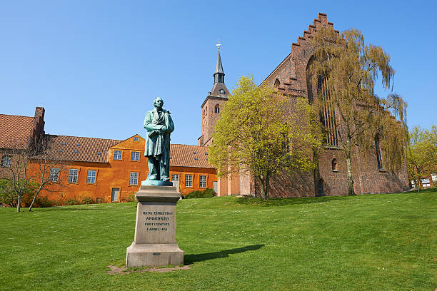 H. C. Andersen And St. Knud's Cathedral Odense, Denmark - April 19, 2014: St. Canute's Cathedral. This is the park-side toward "The Fairy Tale Garden" away from the city center. The statue is the poet Hans Christian Andersen. it is an early day in spring. statue of hans christian andersen stock pictures, royalty-free photos & images