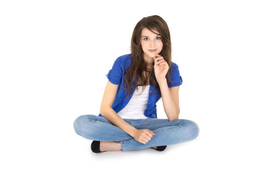Attractive brunette female trainee sitting in crossed legs on the floor isolated over white background.