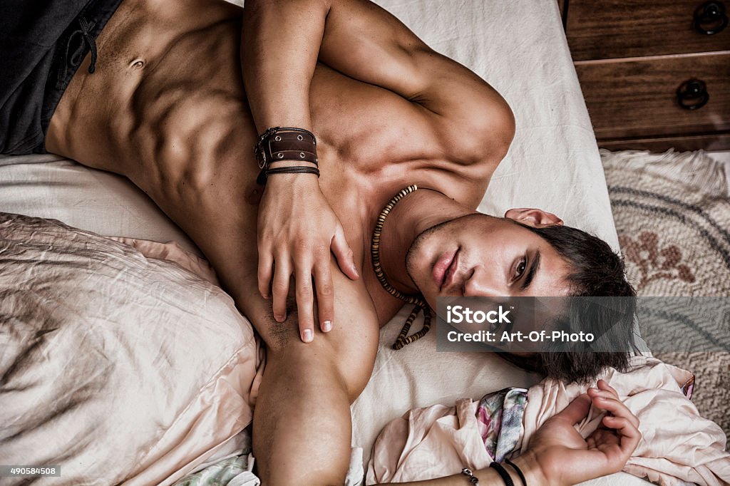 Shirtless sexy male model lying alone on his bed Shirtless sexy male model lying alone on his bed in his bedroom, looking at camera with a seductive attitude Men Stock Photo