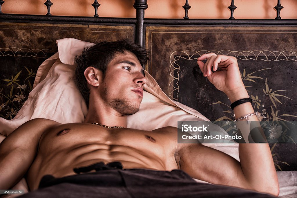 Shirtless sexy male model lying alone on his bed Shirtless sexy male model lying alone on his bed in his bedroom, looking away with a seductive attitude 2015 Stock Photo