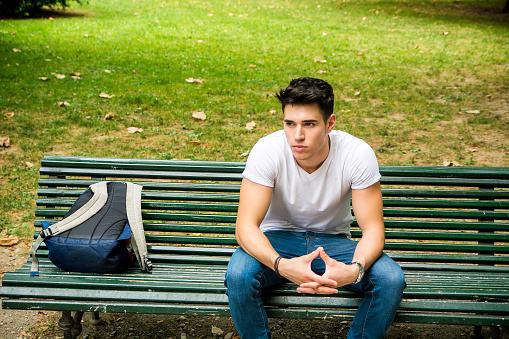 Young Male Student Sitting on Park Bench Seriously