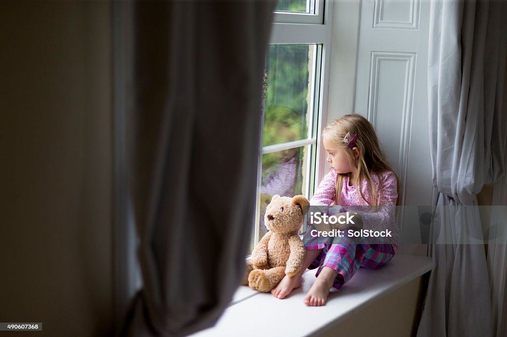 Just wanting a friend to play with. Little girl sits on a window sill alone with her teddy. She is looking out of the window. Child Stock Photo