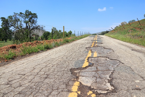 Damaged road of Yokohl Drive in California, USA - cracked asphalt blacktop with potholes and patches