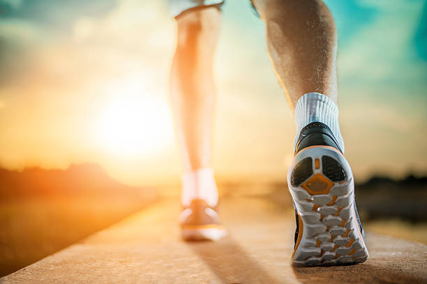Runner Man Feet Running on Road closeup on shoe at sunset with the sun flare at background.