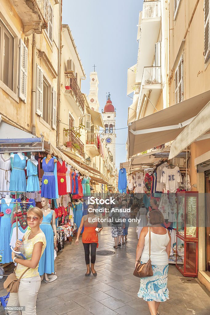 Tourists walking and shopping on narrow streets Kerkyra, Corfu. Greece - September 16, 2013: Tourists walking and shopping on narrow streets with bell tower of Saint Spiridon church in background. It is single-nave basilica and its bell tower is highest in Ionian Islands and most famous church in Corfu Ancient Stock Photo