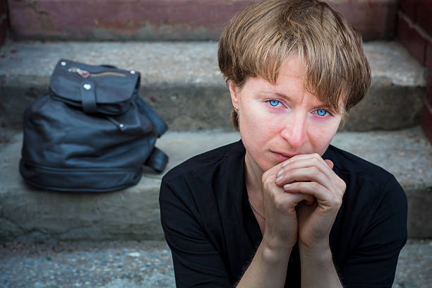 A woman sits on the concrete stairs in a very depressed mood, lying next to her on the stairs of her backpack.