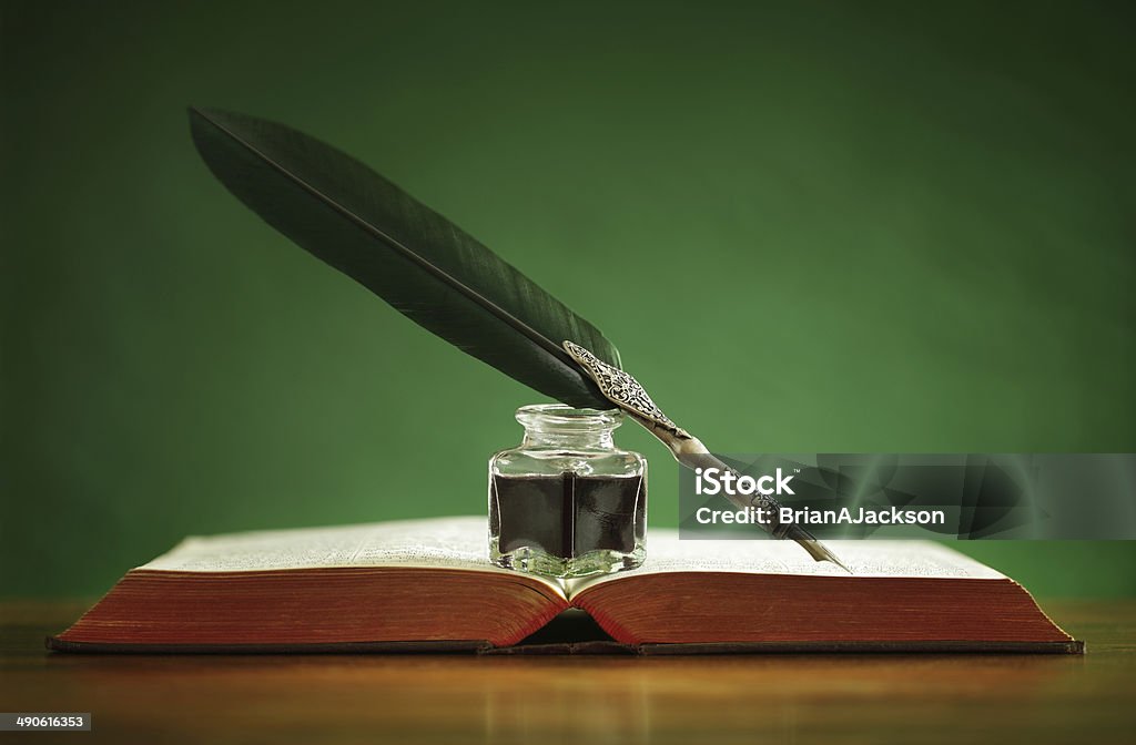Quill pen and inkwell on old book Quill pen and inkwell resting on an old book with green background concept for literature, writing, author and history Quill Pen Stock Photo