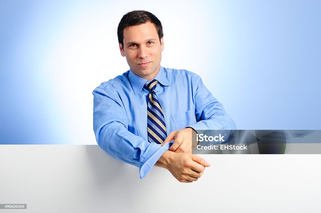 Businessman with Blank Sign Thirty-something businessman leaning on blank white sign rolling up sleeves against blue background Rolling Stock Photo