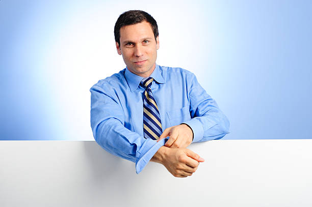 Businessman with Blank Sign Thirty-something businessman leaning on blank white sign rolling up sleeves against blue background rolled up sleeves stock pictures, royalty-free photos & images