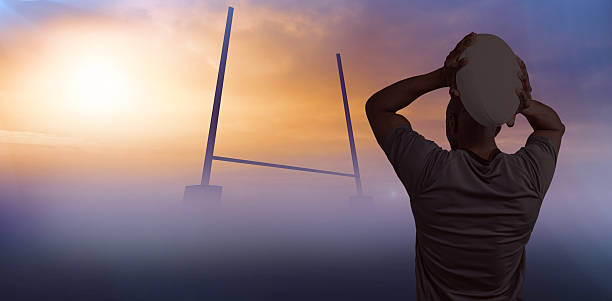 Rear view of sportsman throwing rugby ball against goals posts