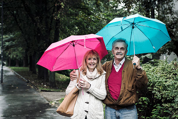 velho casal com guarda-chuvas na chuva - umbrella senior adult couple autumn imagens e fotografias de stock