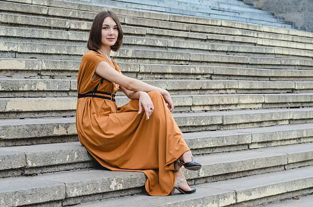 Beautiful dark-haired girl in a long dress sitting on stairs